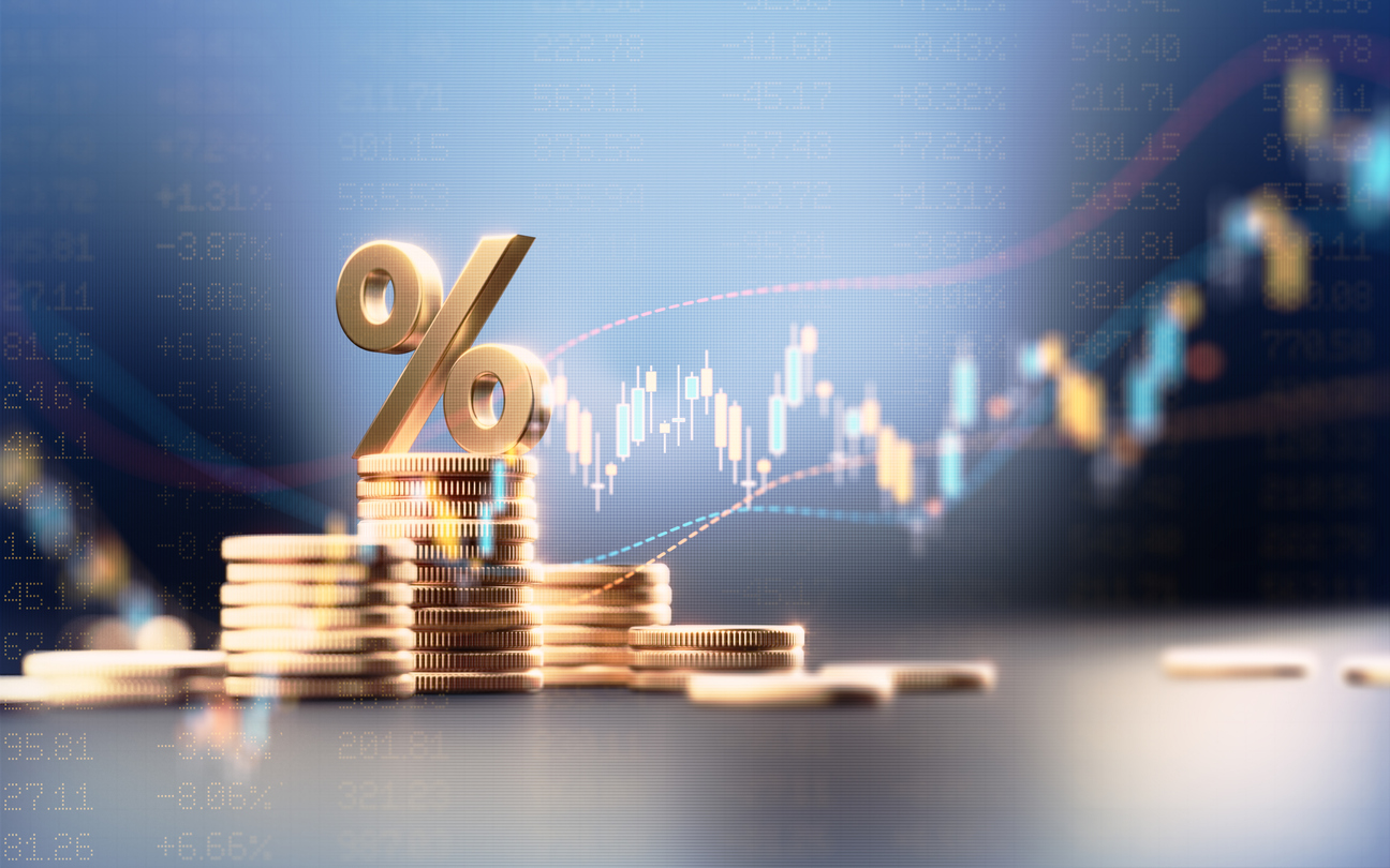 Golden percentage sign atop stacks of coins with stock market charts and numbers in background.